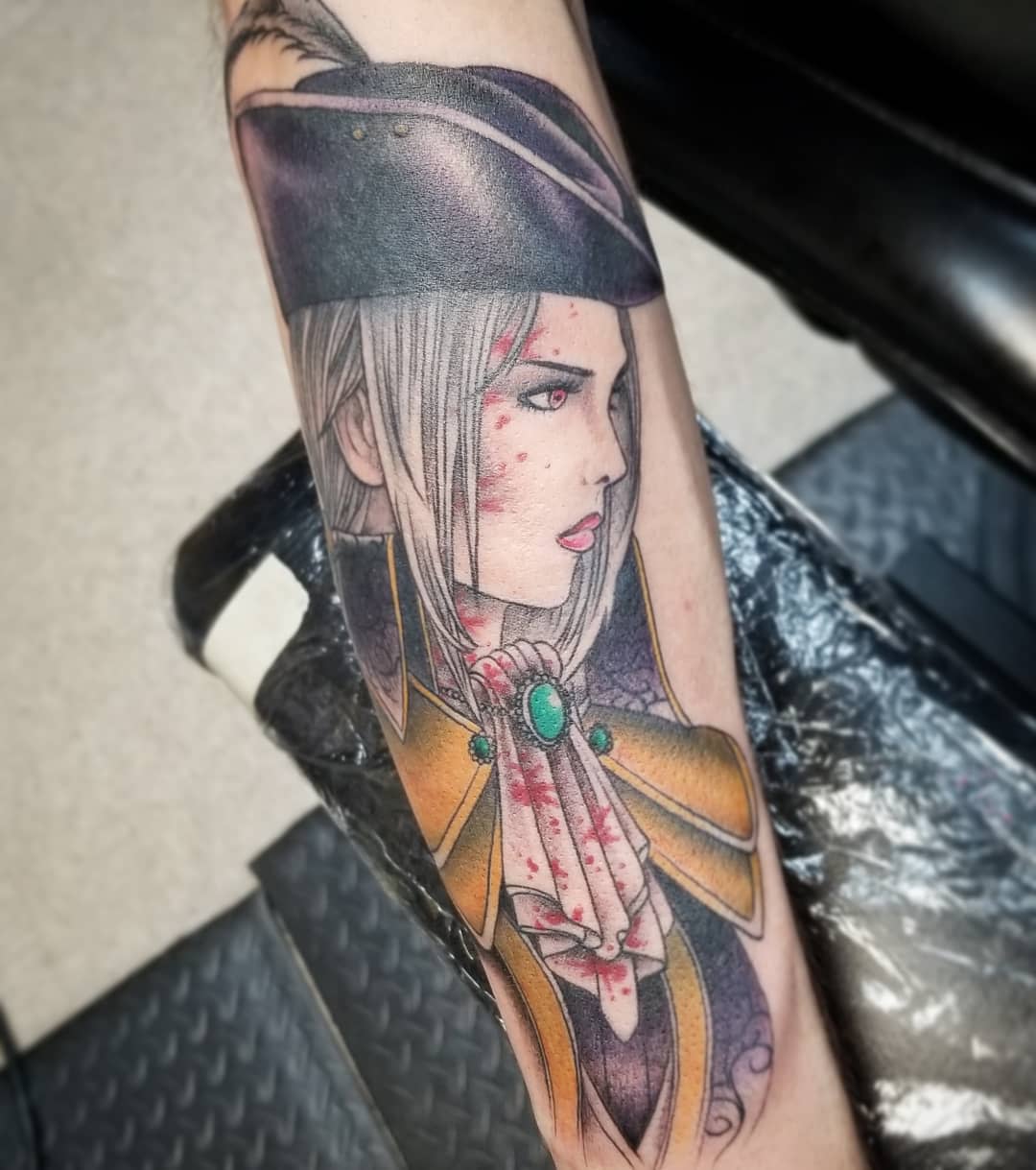 Tattoo of Lady Maria in a striking profile, featuring bold colors and blood-red accents on the forearm